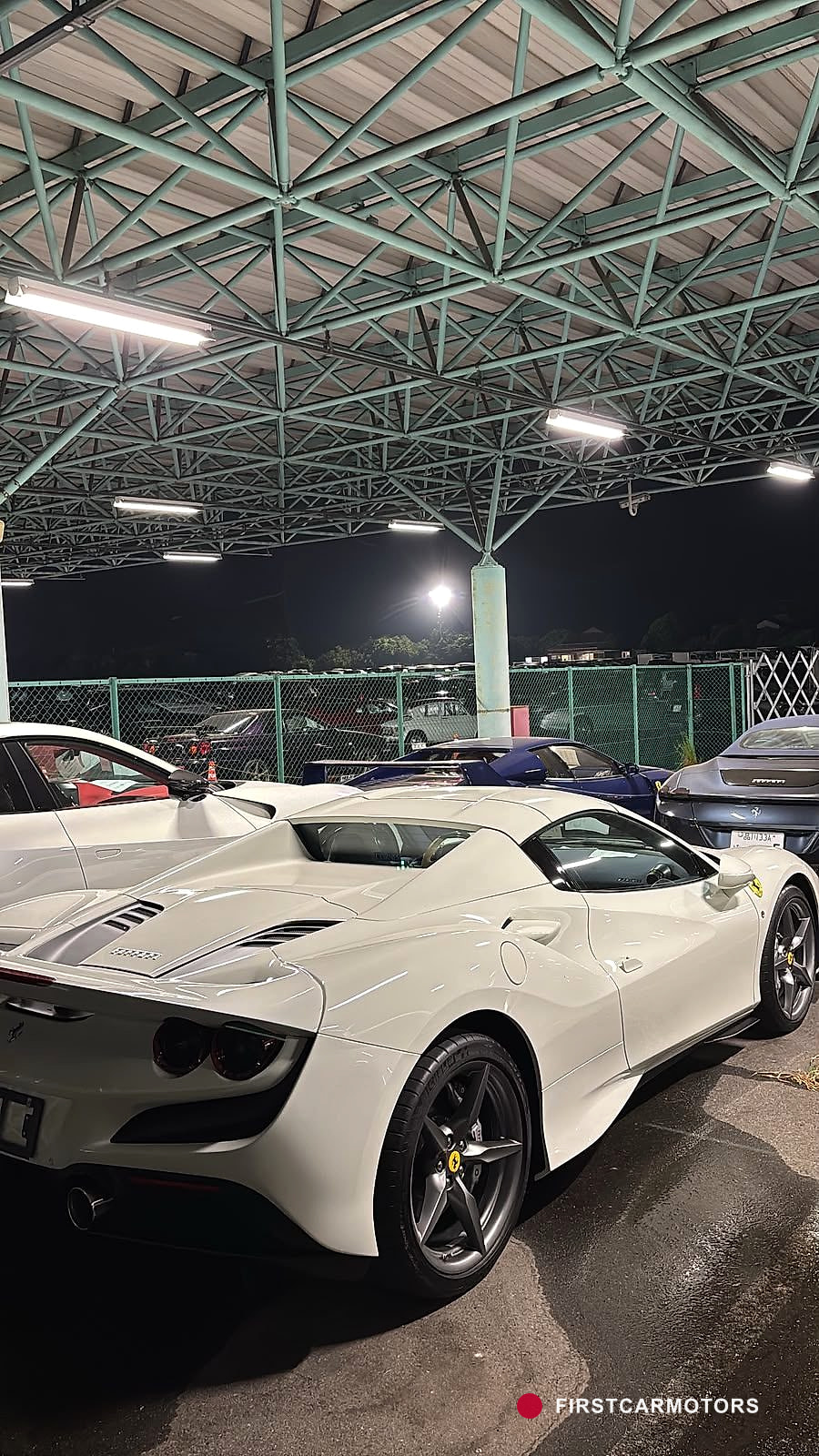 Exklusive Sportwagen, darunter ein Ferrari, stehen dicht geparkt in einer überdachten Auktionshalle.